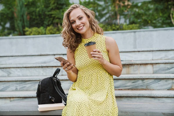 Femme assise à l'extérieur à boire du café à l'aide d'un téléphone mobile . — Photo