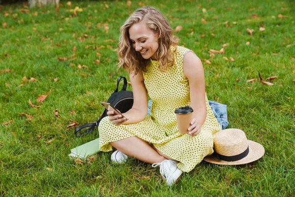 Весела жінка сидить на траві за допомогою мобільного телефону . — стокове фото