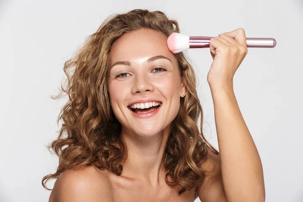 Imagen de la divertida mujer semidesnuda sonriendo y usando un cepillo de maquillaje —  Fotos de Stock