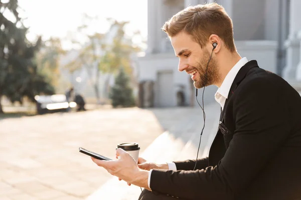 Hadsome young businessman wearing earphones standing — Stock Photo, Image