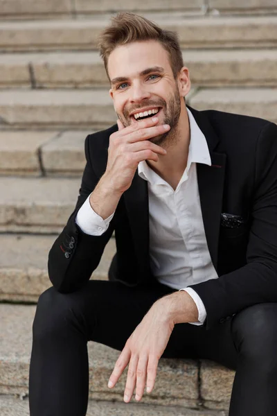 Guapo joven sonriente hombre de negocios sentado en los escalones — Foto de Stock