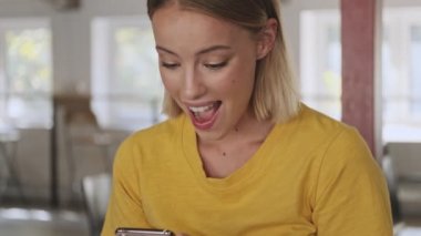 A happily surprised woman is using a smartphone while waiting in a conference hall