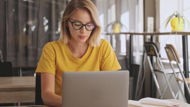 Skoncentrowana Blondynka Okularach Żółtej Koszulce Pracuje Laptopie Siedząc Sali Konferencyjnej — Wideo stockowe