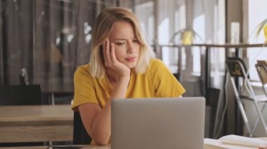 A serious unpleased young woman is working on her laptop in a conference hall