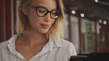A cropped view of a smiling woman wearing eyeglasses is using a laptop and cellphone while sitting in a conference hall