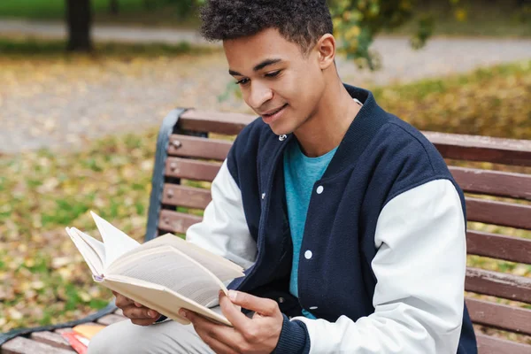 Smiling african boy student sitting on a bench at the park — Stock Photo, Image