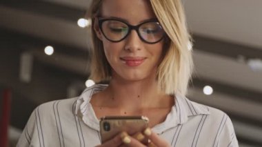 A close-up view of a smiling woman wearing eyeglasses is using a phone while sitting in a conference hall