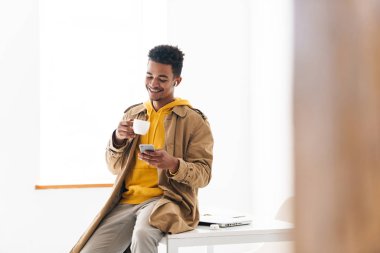 Afro-Amerikan bir adamın cep telefonu kullanıp kahve içerkenki fotoğrafı.