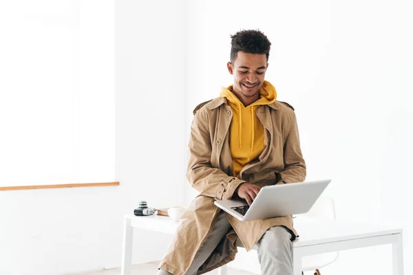 Fénykép afro-amerikai férfi segítségével laptop és mosolyog, miközben ül — Stock Fotó