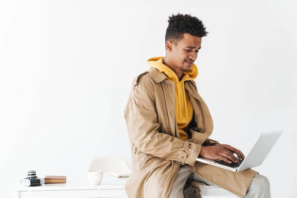 Photo d'un homme afro-américain confus tapant sur un ordinateur portable assis — Photo