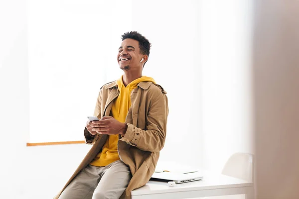 Foto de hombre afroamericano riéndose usando teléfono celular y auricular — Foto de Stock