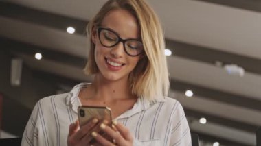 A beautiful smiling woman wearing eyeglasses is using a phone in a conference hall