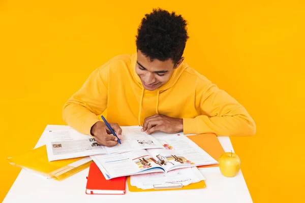 Menino adolescente africano feliz estudando enquanto sentado na mesa — Fotografia de Stock