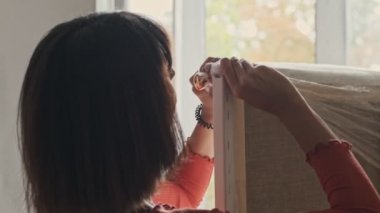 Close-up view of the attractive caucasian young woman in brown t-shirt uncovering an easel