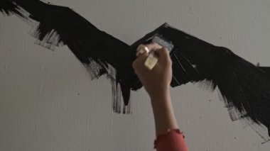 Cropped view of the attractive caucasian young woman in brown t-shirt drawing with a brush on an easel