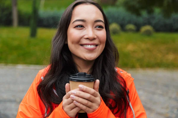 Glimlachende jonge aziatische vrouw dragen regenjas wandelen buiten — Stockfoto