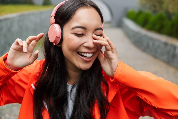 Smiling young asian woman wearing raincoat walking outdoors — Stockfoto