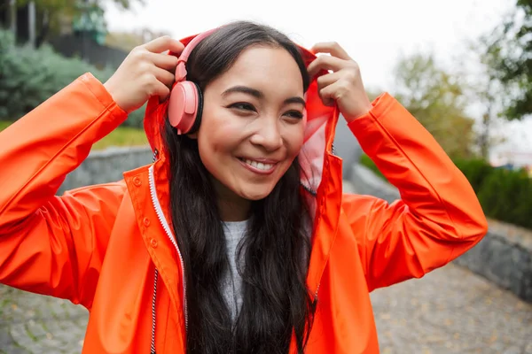 Souriant jeune asiatique femme portant imperméable marche à l'extérieur — Photo