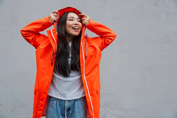 Smiling young asian woman wearing raincoat walking outdoors — Stockfoto
