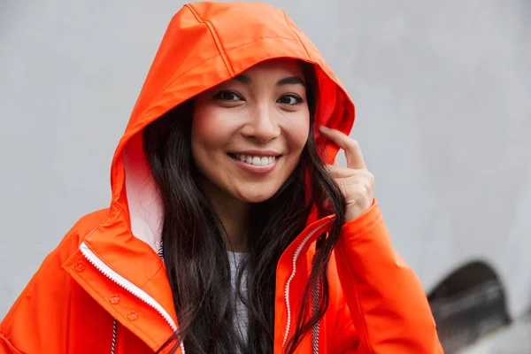 Smiling young asian woman wearing raincoat walking outdoors
