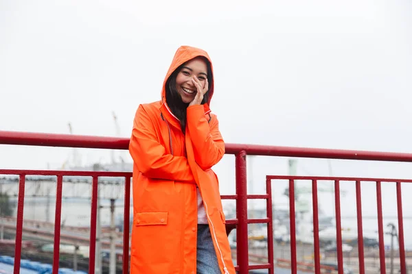 Smiling young asian woman wearing raincoat walking outdoors — Stockfoto