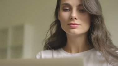 A nice focused young woman is using a laptop computer indoors