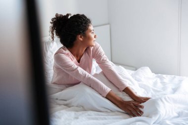 Smiling beautiful young african woman sitting in bed