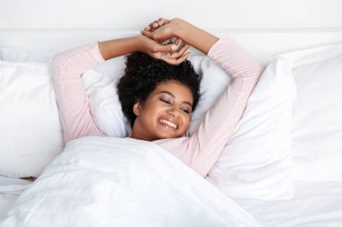 Smiling beautiful young african woman laying in bed in the morning