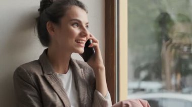 Güzel ve şık genç bir kadın pencerenin yanında otururken birini arıyor.