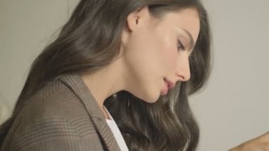 Ciddi derecede çekici genç bir kadın elinde dizüstü bilgisayarla masada otururken belgelere bakıyor.