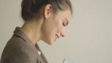 Güzel genç bir iş kadınının yan görüntüsü beyaz duvar arkasında izole edilmiş belgeler tutuyor.