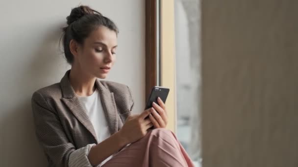 Nice Young Woman Using Her Smartphone While Sitting Window — Stock Video