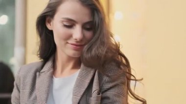 Cilveli bir kadın dışarıda dikilirken saçına dokunuyor.