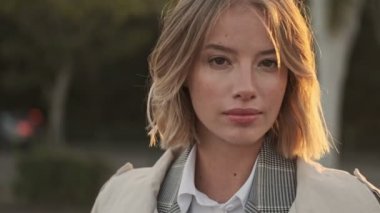 Ceketli mutlu sarışın iş kadını kameraya bakıyor ve havaalanının yakınındaki park yerinde eğleniyor.