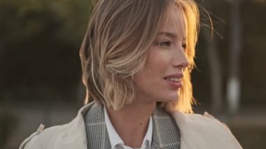 Ceketli, gülümseyen sarışın iş kadını kameraya bakıyor ve havaalanının yakınındaki otoparkta eğleniyor.