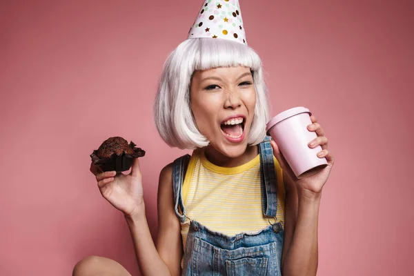 Kép ázsiai lány visel party kúp iszik kávét és eszik — Stock Fotó