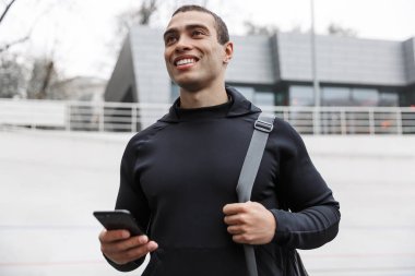 Yakışıklı, gülümseyen bir sporcu spor çantası taşıyor.