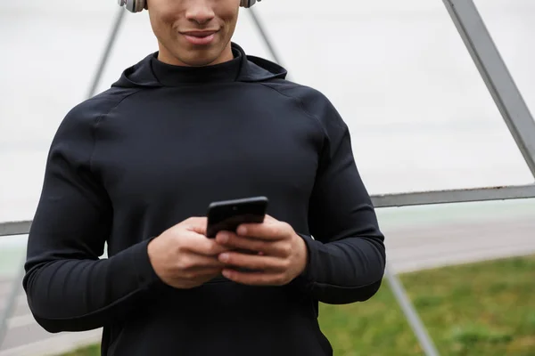 Foto do atlético sorrindo esportista usando fones de ouvido e celular — Fotografia de Stock