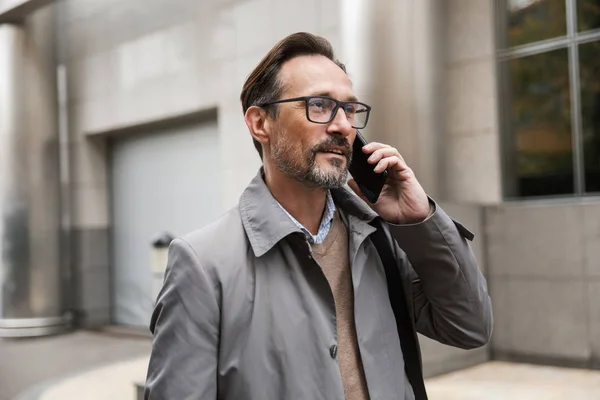 Image of pleased businessman talking on cellphone while standing — Stock Photo, Image