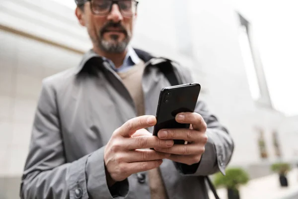 Imagen de un hombre de negocios adulto serio usando el teléfono celular mientras está de pie — Foto de Stock