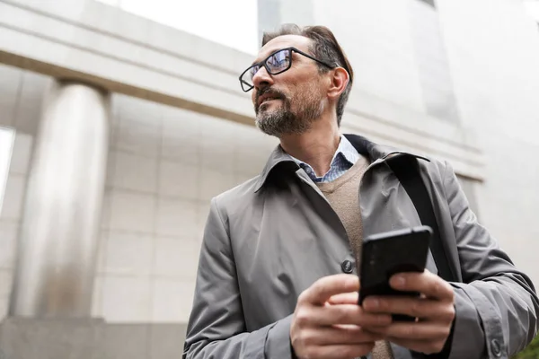 Imagen de un hombre de negocios adulto serio usando el teléfono celular mientras está de pie — Foto de Stock