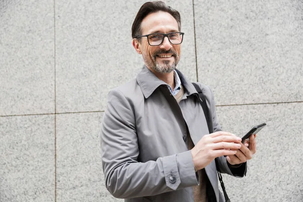 Зображення щасливого дорослого бізнесмена, який використовує мобільний телефон, стоячи — стокове фото