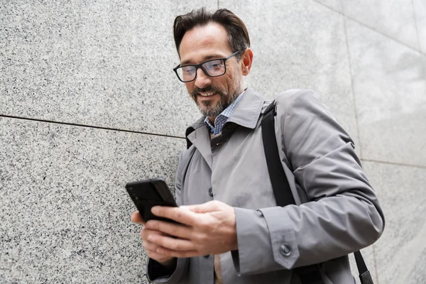 Imagen de hombre de negocios adulto alegre usando el teléfono celular y sonriendo — Foto de Stock