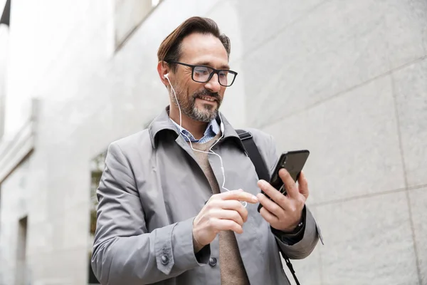 Imagen del hombre de negocios alegre usando el teléfono celular y los auriculares — Foto de Stock