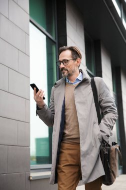 Olgun memnun iş adamının yürürken cep telefonu tutuşu