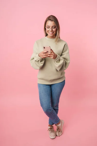 Retrato de jovem mulher engraçada em óculos usando celular e sorrindo — Fotografia de Stock