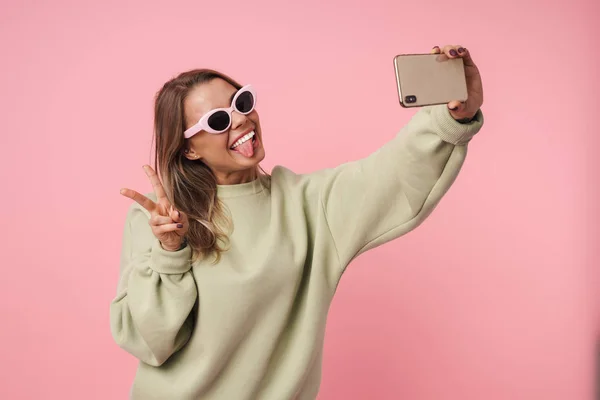 Retrato de una mujer agradable y divertida usando el teléfono celular y el gesto de señal de paz — Foto de Stock