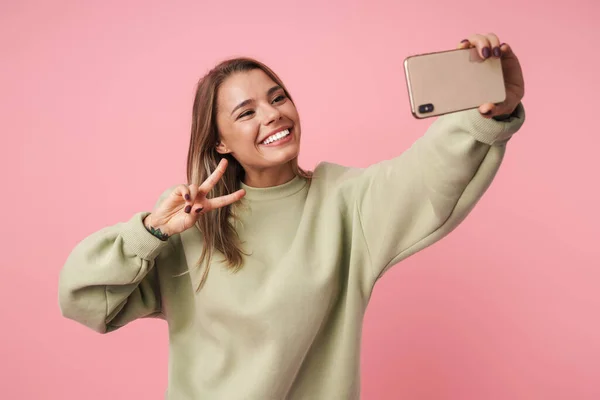 Retrato de una linda mujer sonriente usando un teléfono celular y un gesto de paz — Foto de Stock