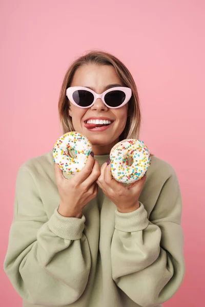 Porträt einer amüsanten Frau, die Donuts hält und die Zunge herausstreckt — Stockfoto