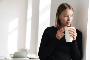 Blonde business woman in office indoors drinking hot tea.